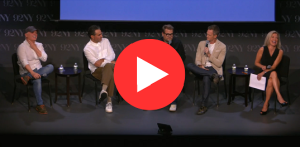 A group of five people sits on a stage for a panel discussion. They are casually dressed, each holding microphones. The atmosphere is relaxed and cheerful.