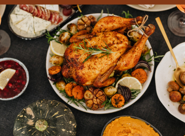 Festive table setting with a roasted chicken centerpiece, surrounded by plates of cheese, mushrooms, cranberries, and glasses of wine, evoking warmth.