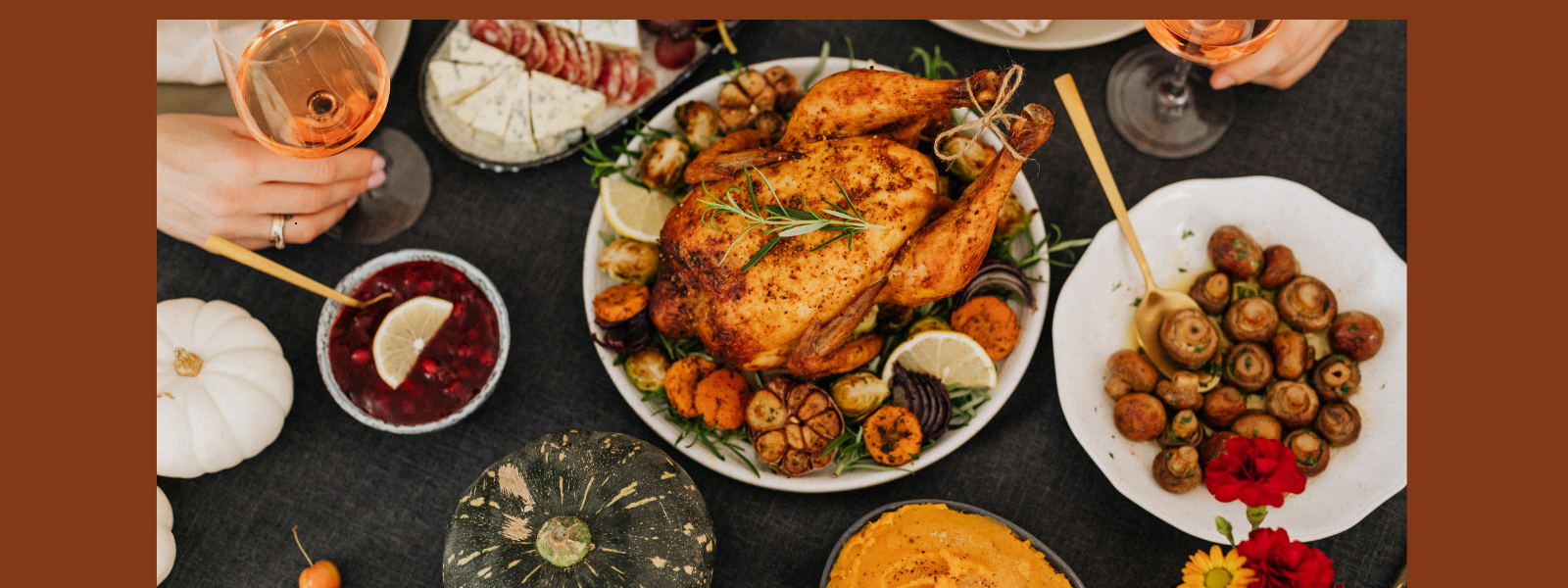 Festive table setting with a roasted chicken centerpiece, surrounded by plates of cheese, mushrooms, cranberries, and glasses of wine, evoking warmth.