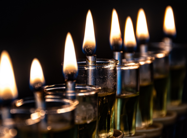 Alt text: "A row of lit oil candles with small flames in glass holders against a dark background, conveying warmth and tranquility."