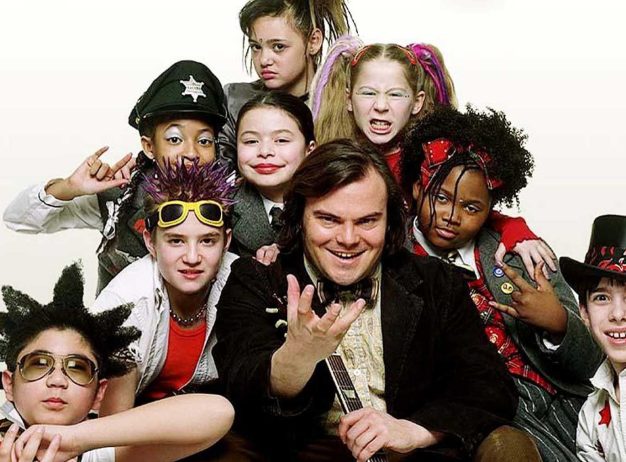 A group of children in colorful costumes stands with a man in a suit, all smiling or making playful faces, conveying excitement and camaraderie.