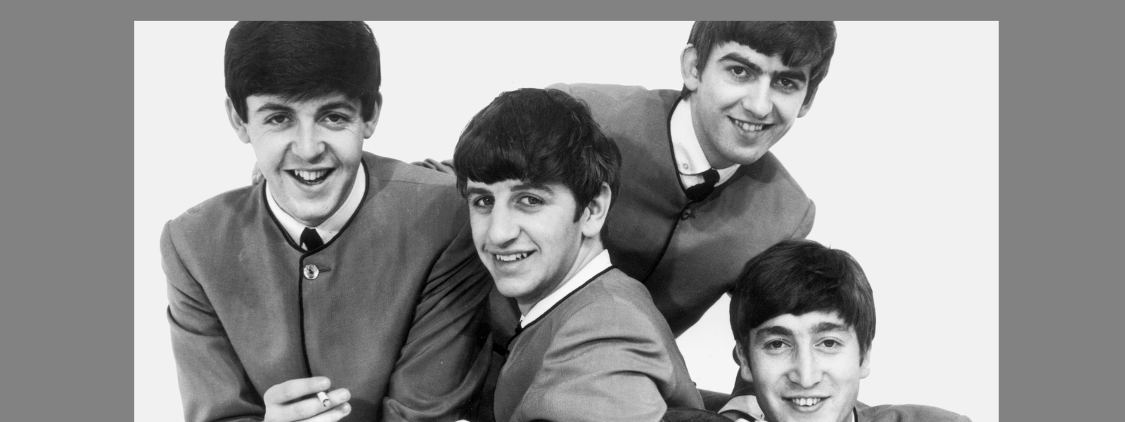 Four young men in 1960s-style suits, smiling and posing together. The mood is cheerful and lively, conveying a sense of camaraderie and fun.