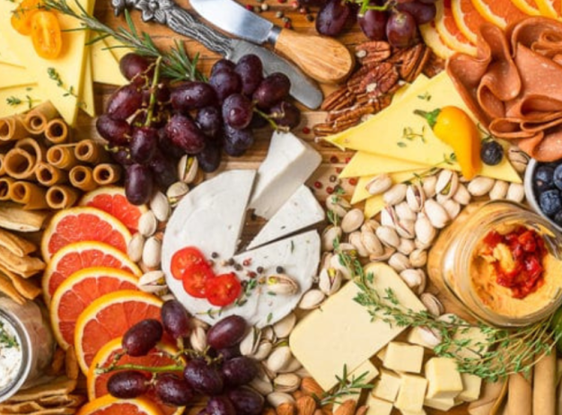 A vibrant charcuterie board with assorted cheeses, cold cuts, grapes, berries, citrus slices, nuts, crackers, and dips, creating a colorful and inviting spread.
