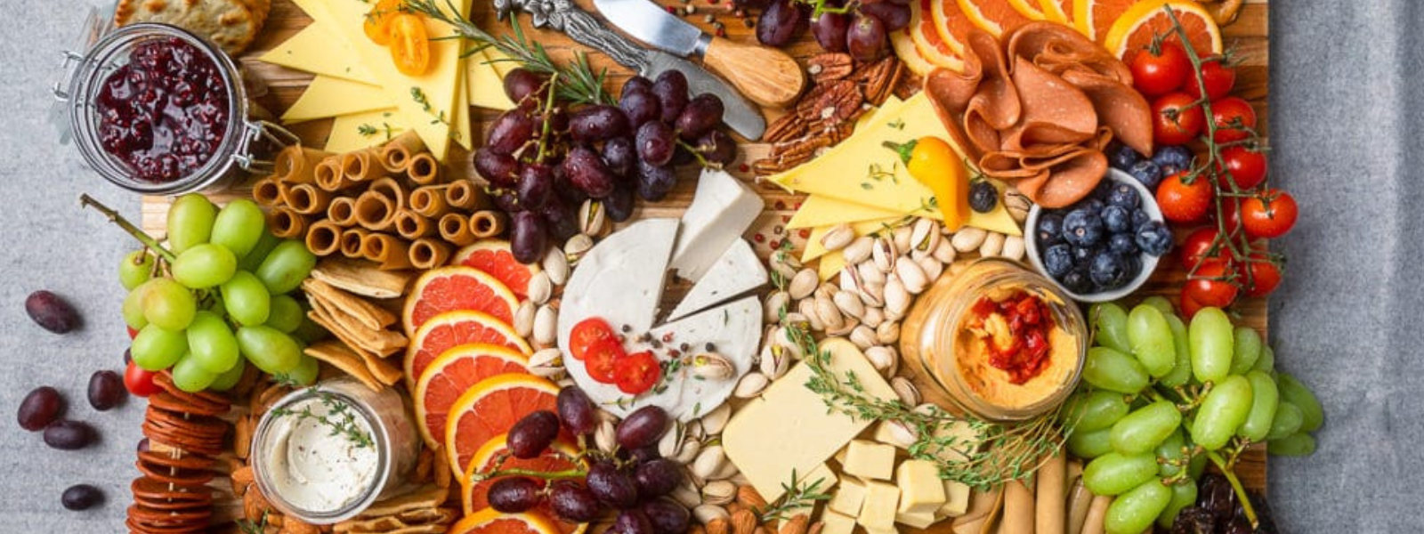 A vibrant charcuterie board with assorted cheeses, cold cuts, grapes, berries, citrus slices, nuts, crackers, and dips, creating a colorful and inviting spread.