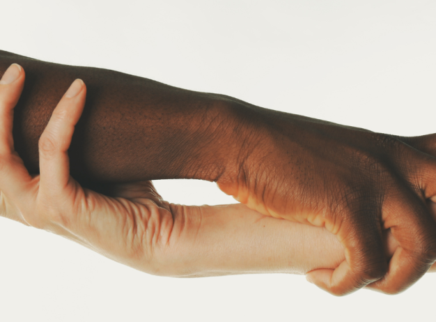 Two hands of different skin tones gently hold each other's forearms against a white background, symbolizing unity and support.