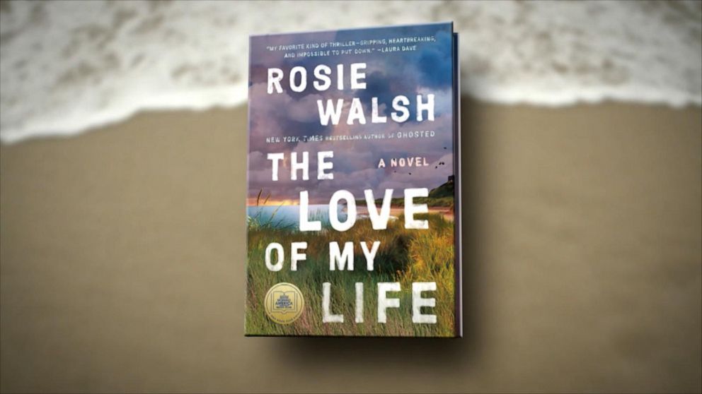 Book cover of "The Love of My Life" by Rosie Walsh on a sandy beach background. The cover depicts a coastal scene with grass and a purple sky.