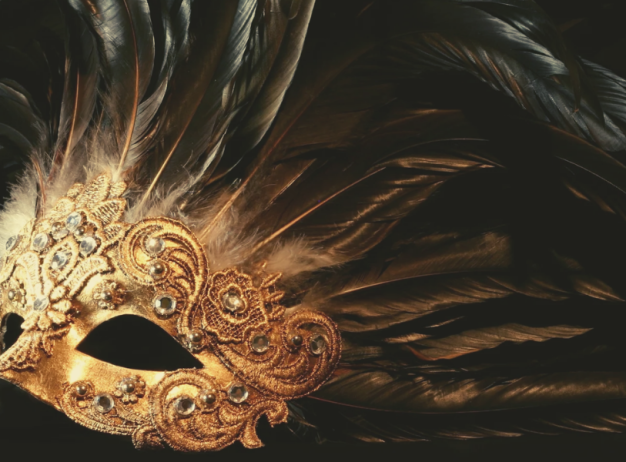 Ornate gold masquerade mask adorned with intricate patterns and dark feathers set against a black background, evoking a sense of mystery and elegance.