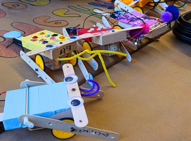 A colorful, custom-built robot made from popsicle sticks, googly eyes, and various small craft items on a table, conveying a fun and creative vibe.