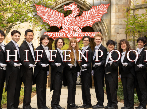 Group of 14 people in formal black suits stand in a line outside, smiling. They wear white gloves. "Whiffenpoofs" text overlays the image with an archway in the background.